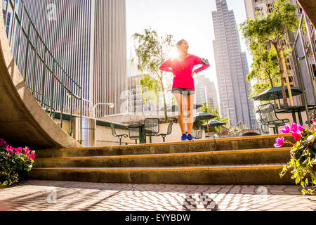 Runner standing on city steps near high rise buildings Stock Photo