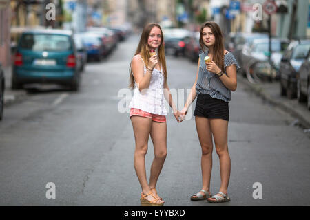 Two teen girls with ice cream stand on the street holding hands. Stock Photo