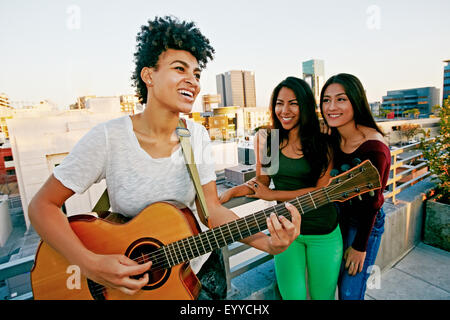 Woman playing guitar for friends on urban rooftop Stock Photo