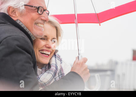 Older Caucasian couple standing under umbrella Stock Photo