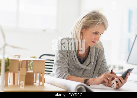 Older Caucasian architect using cell phone in office Stock Photo