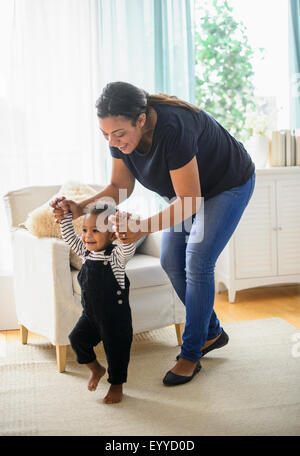 Mixed race mother helping baby son walk in living room Stock Photo