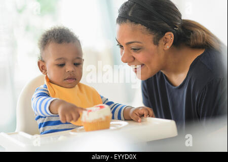 Mixed race mother giving baby son cupcake in high chair Stock Photo