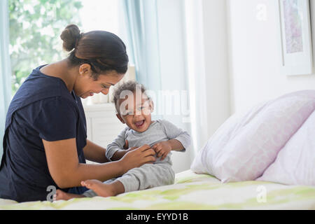 Mixed race mother tickling baby son on bed Stock Photo