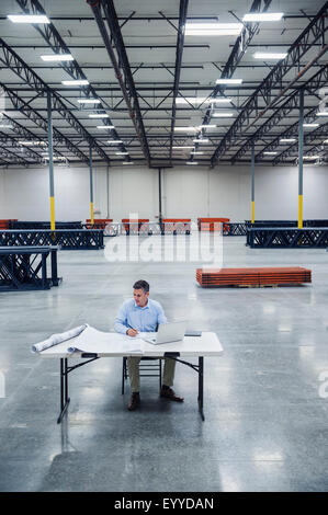 Caucasian architect reading blueprints in warehouse Stock Photo