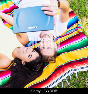 Hispanic couple taking selfie on blanket in park Stock Photo