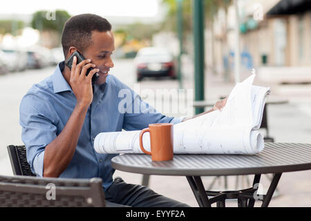 Black architect talking on cell phone and reading blueprints Stock Photo