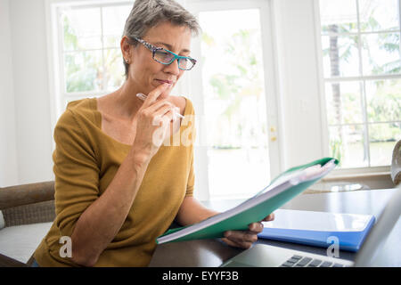 Woman reading folder at desk in living room Stock Photo