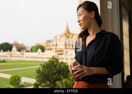 Asian businesswoman admiring view from cafe window, Phnom Penh, Cambodia Stock Photo