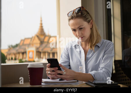 Caucasian businesswoman using cell phone in cafe, Phnom Penh, Cambodia Stock Photo