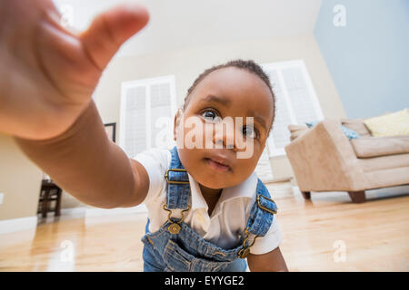 Black baby reaching for camera on living room floor Stock Photo