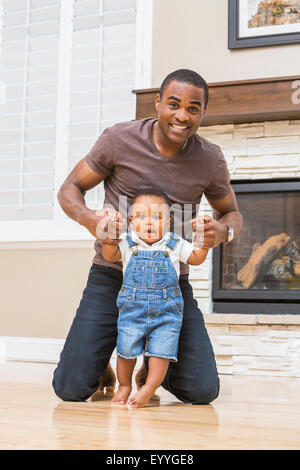 Black father helping baby son walk on living room floor Stock Photo