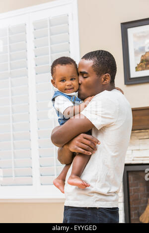 Black father kissing baby son in living room Stock Photo