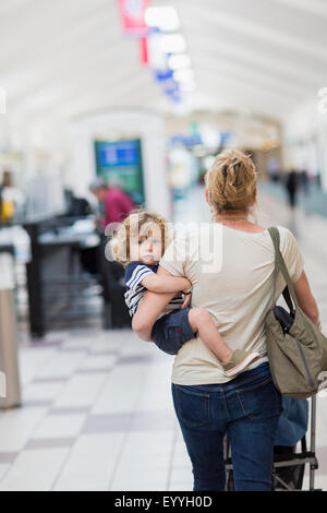 Caucasian mother carrying baby son in airport Stock Photo