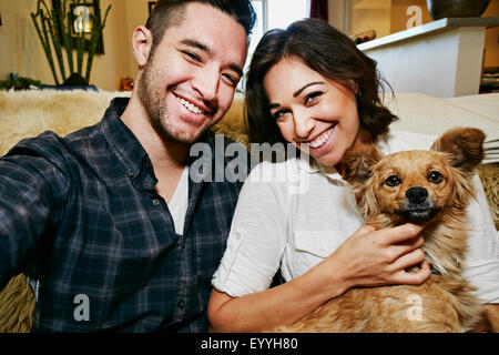 Couple holding dog on sofa in living room Stock Photo