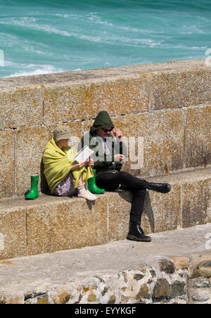 Man and woman sheltering from wind on seafront at St Ives, Cornwall, England, UK Stock Photo