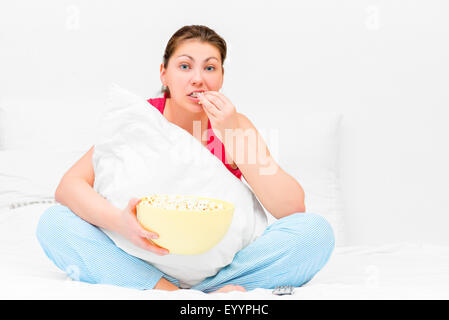 Brunette attentively watching television and eating popcorn Stock Photo