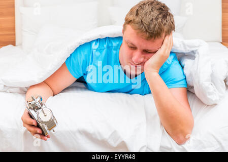 annoyed man with an alarm clock in the hands of suffering from insomnia Stock Photo