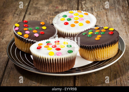 Four cupcakes with dark and white chocolate icing, decorated with smarties, on a plate Stock Photo