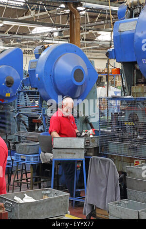 An older male worker manufactures metal components for the construction industry using a large steel pressing machine Stock Photo
