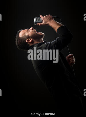 Singer performing with microphone against dark background Stock Photo