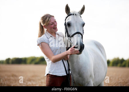 A young woman standing in a wheat field with a horse, laughing Stock Photo