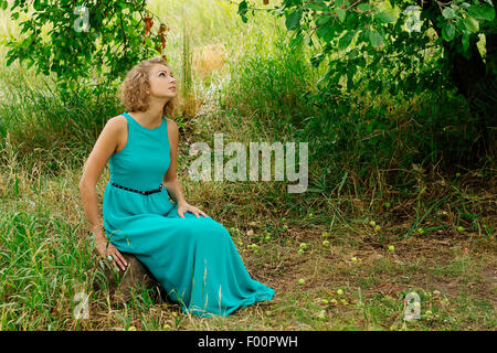 Young woman in blue dress sitting under apple tree selective focus horizontal Stock Photo