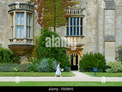 Young girl walking past Lacock Abbey, a National Trust property in Wiltshire, England UK Stock Photo