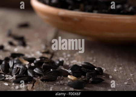 Roasted and salted sunflowers seeds in their shells, and bowl over old wood background Stock Photo
