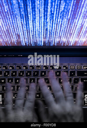 Hands are typing on a laptop computer in the dark with illuminated keyboard and mystic program code on screen Stock Photo