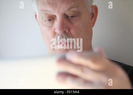 A senior man with a hand on his laptop cover checks his screen. Stock Photo
