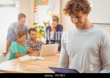 Casual businessman using digital tablet with colleagues behind in office Stock Photo