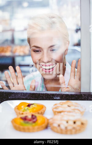 Puzzled pretty woman looking at a fruit pie through the glass Stock Photo