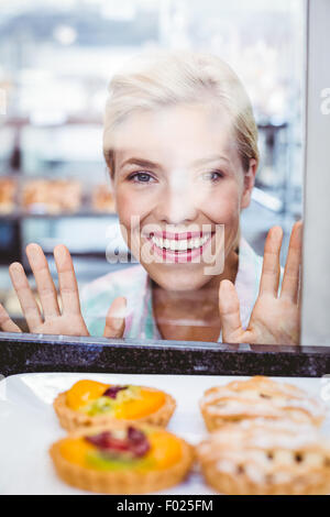 Smiling pretty woman looking at a fruit pie through the glass Stock Photo