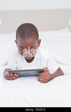 Pretty smiling little boy using digital tablet in bed Stock Photo