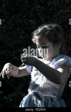 Five year old in a fancy dress in the garden using scissors Stock Photo