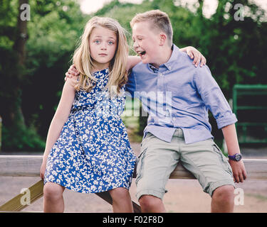 Boy and girl sitting on wooden gate with their arms around each other Stock Photo