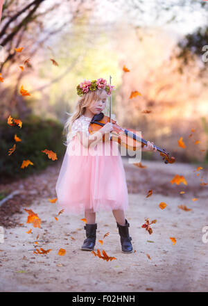 Girl standing in road playing the violin with leaves falling all around, California, USA Stock Photo