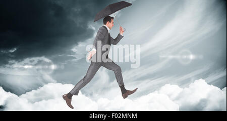 Composite image of businessman jumping holding an umbrella Stock Photo