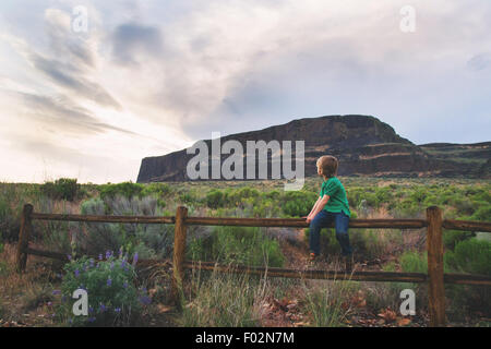 Boy sitting on wooden fence looking over his shoulder Stock Photo