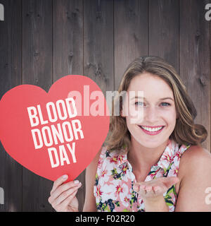 Composite image of woman holding heart card and blowing kiss Stock Photo