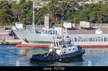 Small tug boat with white superstructure and dark blue hull works in port Stock Photo
