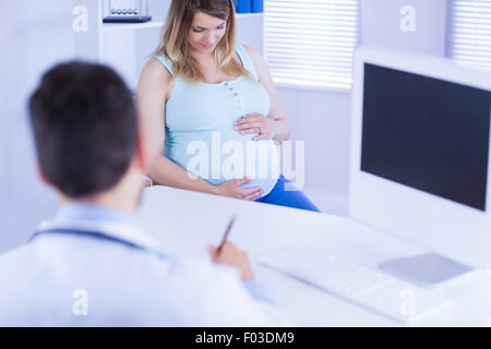 Doctor taking notes while listening to pregnant patient Stock Photo