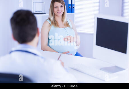 Smiling pregnant patient looking at camera while doctor taking notes Stock Photo
