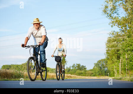 Senior couple riding bikes through summer landscape on a road Stock Photo