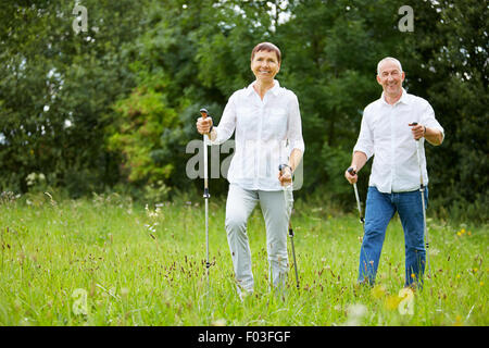 Active senior couple doing nordic walking in summer on a meadow Stock Photo