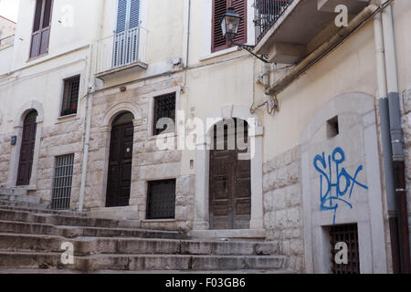 Arched wooden doors, balconies and graffiti on a wall on a narrow street in Andria, Puglia, Italy. Stock Photo