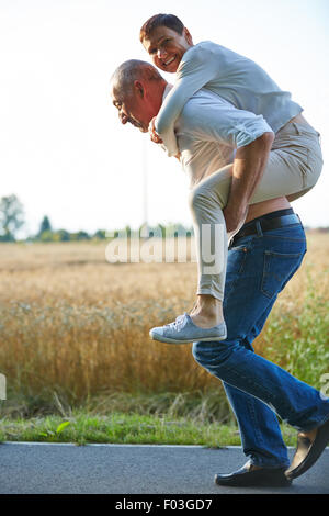 Old man giving woman piggyback ride on his back in summer Stock Photo