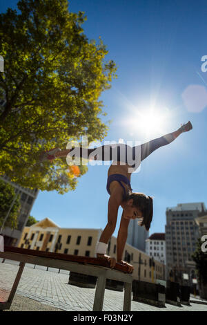 Athletic woman performing handstand and doing split on bench Stock Photo