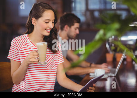 Smiling young woman enjoying latte and using tablet computer Stock Photo
